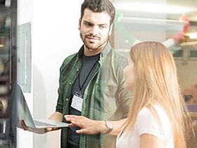 Man holding laptop and explaining something to his teammate