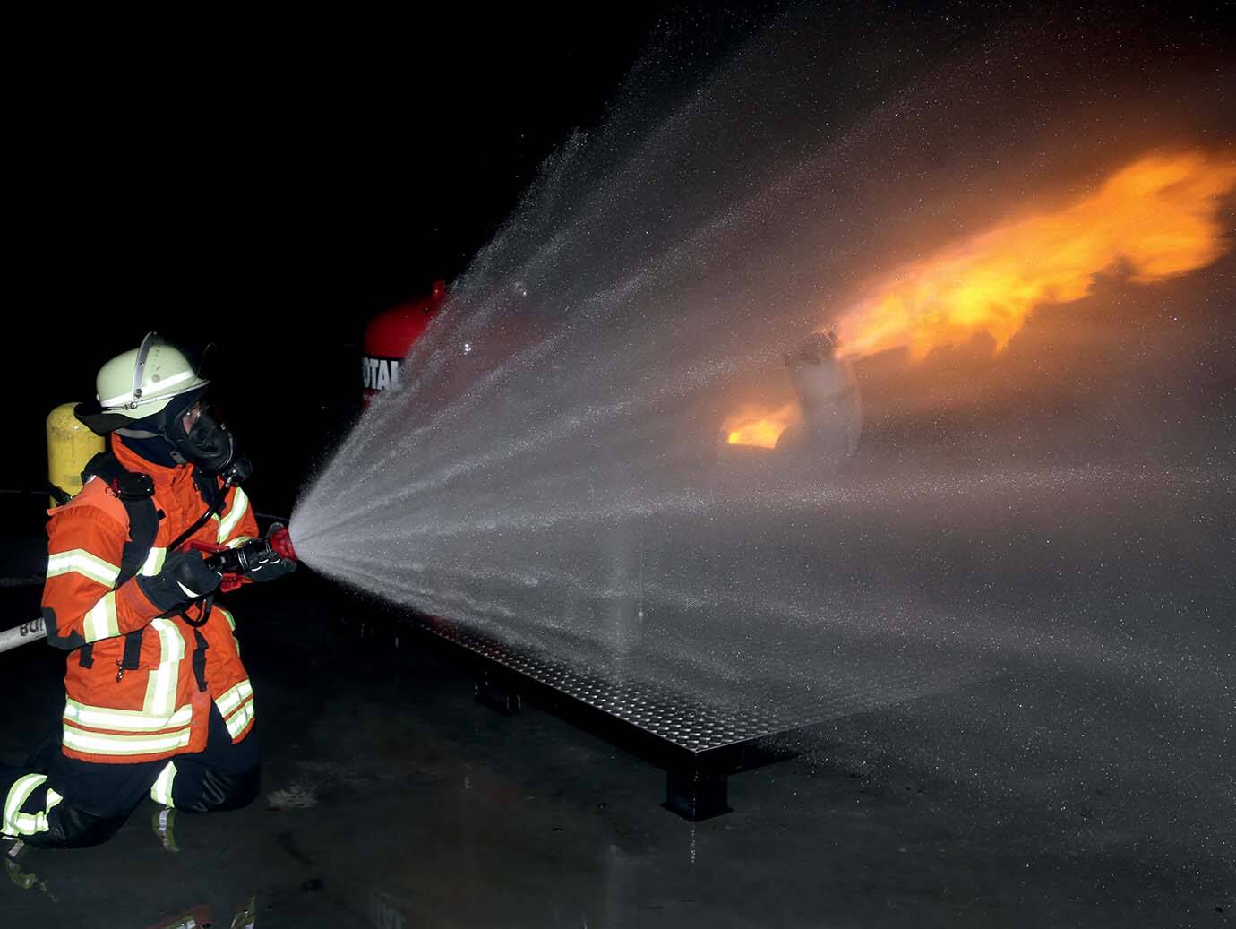Firefighter in suit dousing a flame in an indoor space