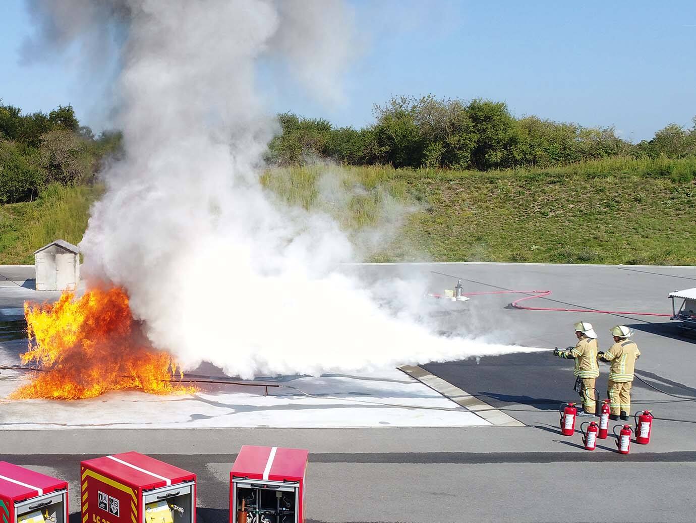 Two firefighters in suit dousing a flame in an outdoor space