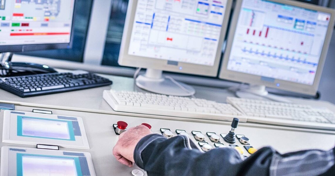 A control panel being operated with data management softwares displayed on computer monitors in the background