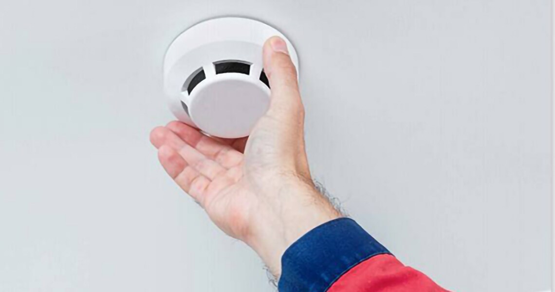 A hand inspecting a roof-mount smoke detector
