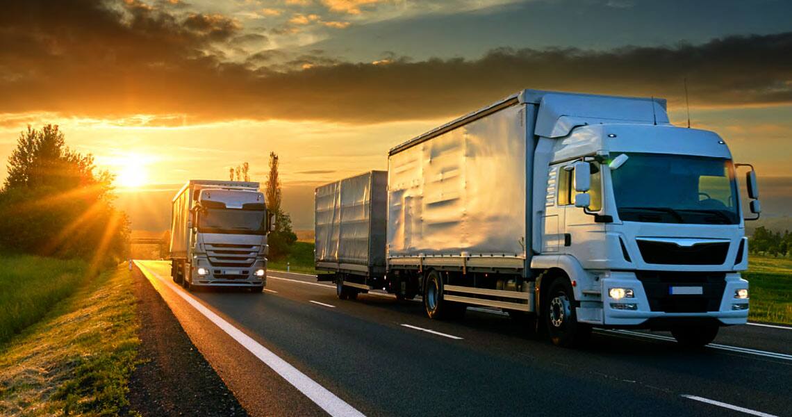 One freight truck overtaking another on a sunlit highway