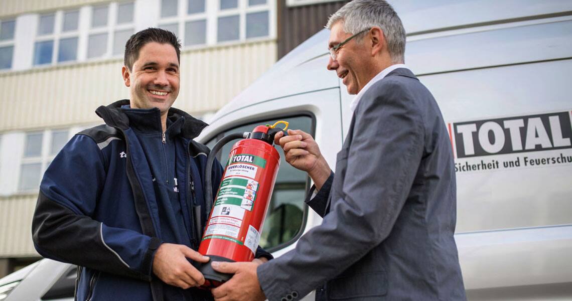 A man handing over a TOTAL-branded fire extinguisher to another man