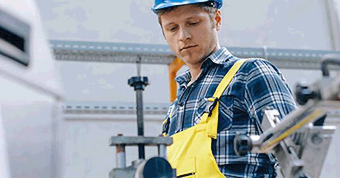 Worker in safety helmet operating an equipment in a factory