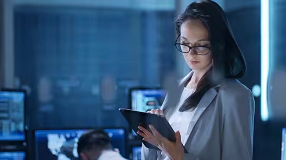 A female employee observing the tab with a background of a security person observing the cctv footages